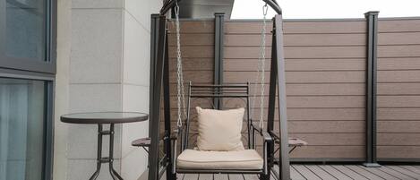 Una terraza de madera con una silla colgante y una pequeña mesa.