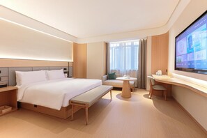 Une chambre d’hôtel moderne, dotée d’un grand lit, d’un bureau, d’un canapé et d’un téléviseur fixé au mur.