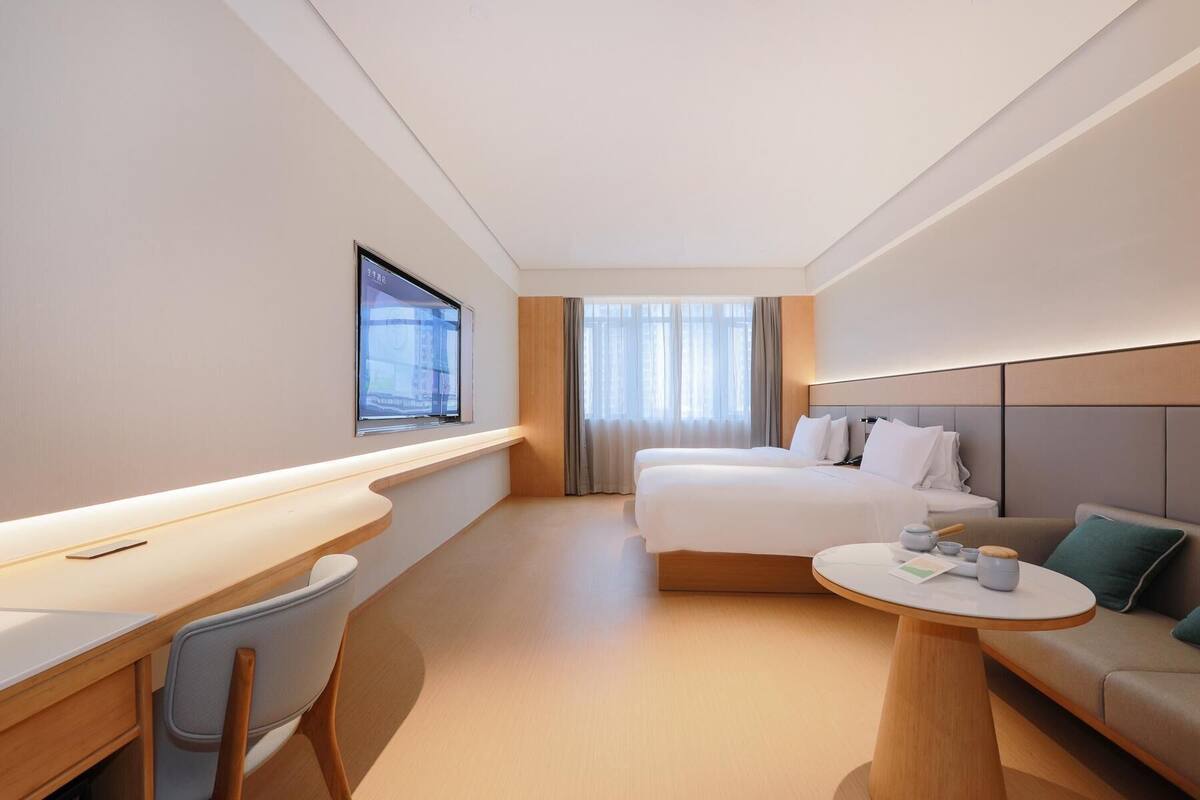 Una habitación de hotel con cama, escritorio, silla, mesa redonda y televisor en la pared.