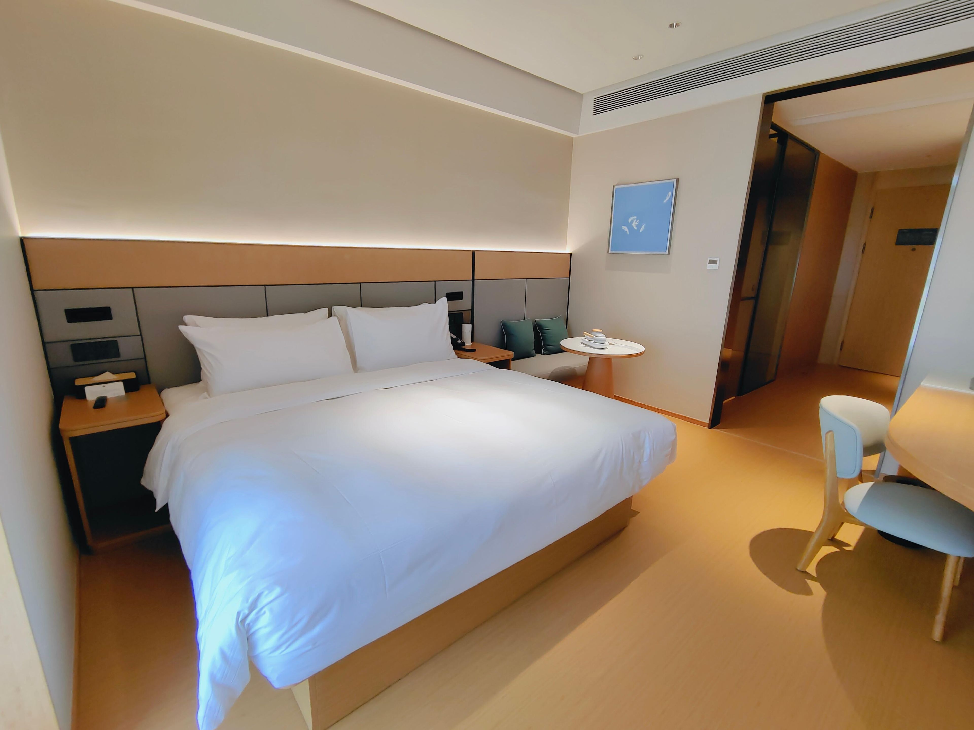 A modern hotel room with a large bed, bedside tables, a round table, and a chair.