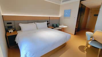 A modern hotel room with a large bed, bedside tables, a round table, and a chair.