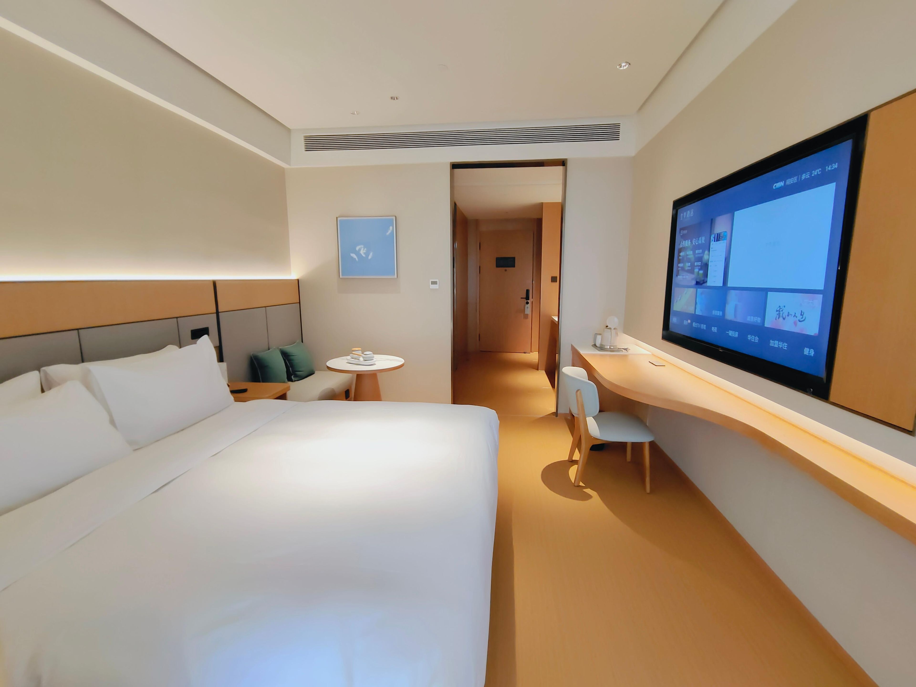 A hotel room with a bed, a desk, a chair, a TV, and a small table.