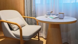 Een kamer met een fauteuil met houten frame, een klein rond tafeltje met een theepot, kopjes en een kaart.