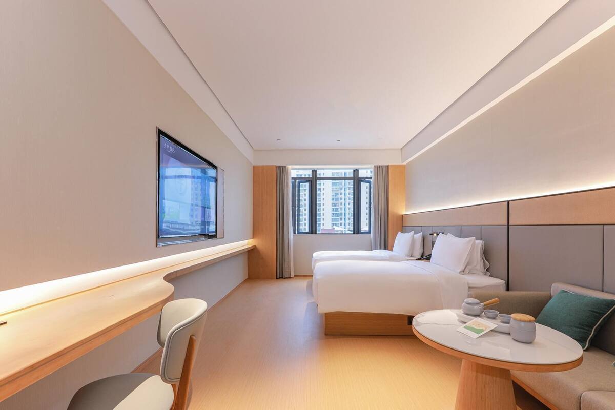 Una habitación de hotel con una cama, un escritorio, una silla, una mesa redonda con tetera y una ventana con vistas a la ciudad.