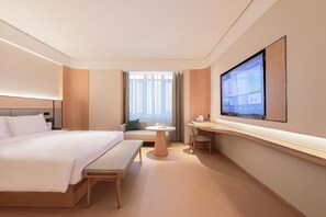 Une chambre d’hôtel avec un grand lit, un bureau, une chaise et un téléviseur fixé au mur.