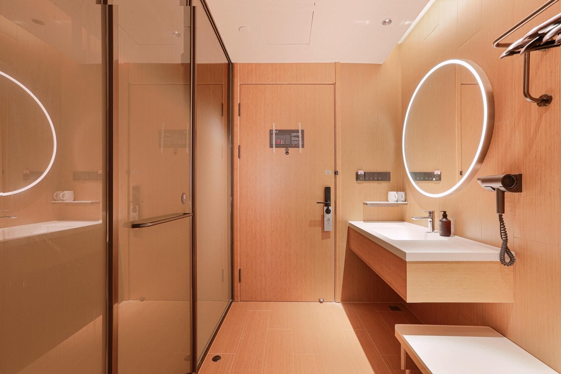 Une salle de bain moderne avec une douche à parois de verre, une porte en bois, un meuble-lavabo avec un miroir et un porte-serviettes.