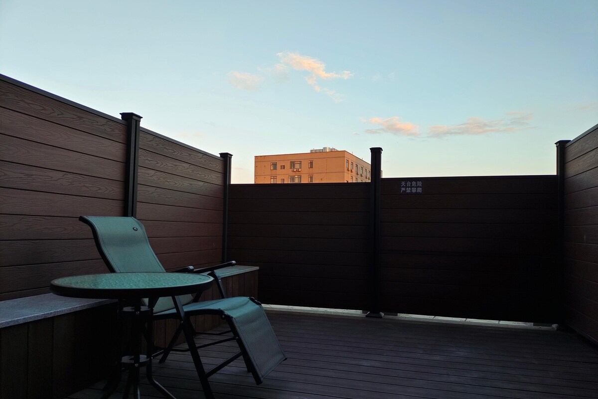 Une terrasse en bois avec une table et deux chaises, une clôture en bois et un bâtiment en arrière-plan.