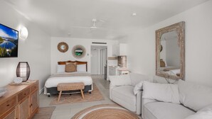 A modern bedroom with a bed, a white sofa, a wooden dresser, a mirror, and a ceiling fan. - Belle Escapes Drift Beachfront Resort Suite 3409 (Palm Cove)