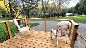 Una terraza de madera con dos sillas, un sendero de grava y vista al lago.