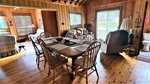 Interior de una cabaña de madera con una mesa de comedor, sillas, un sofá y un área separada para el baño.