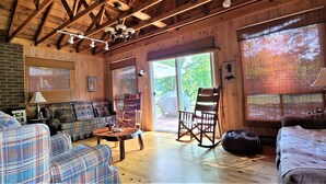 Un acogedor interior de cabaña con un sofá de cuadros, sillones mecedores y una mesa de comedor de madera.