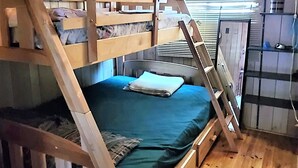 Habitación con literas de madera, una escalera, un escritorio pequeño y una ventana con persianas.