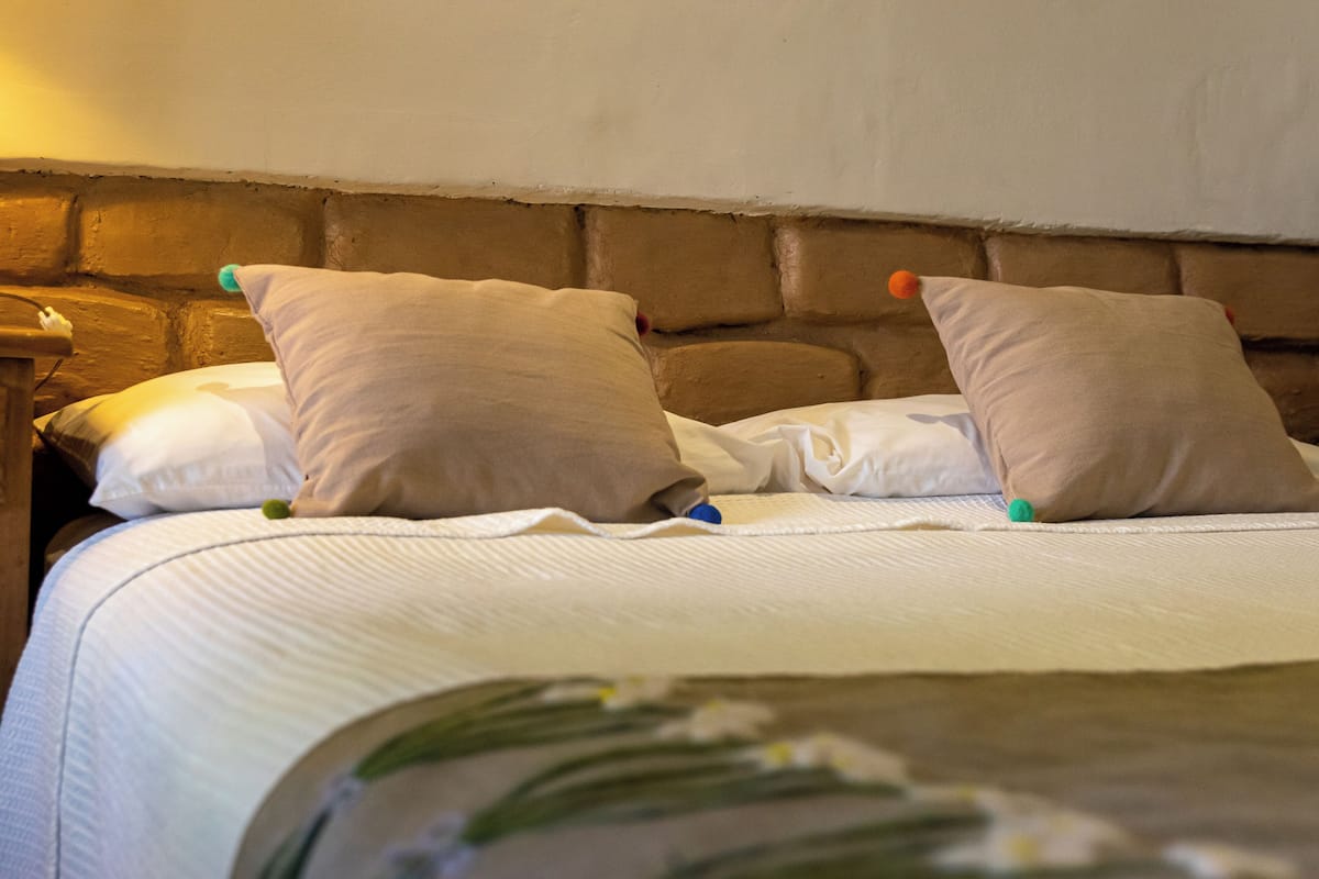 A neatly made bed with white linens and two beige pillows, a wooden headboard, and a bedside table with a lamp.