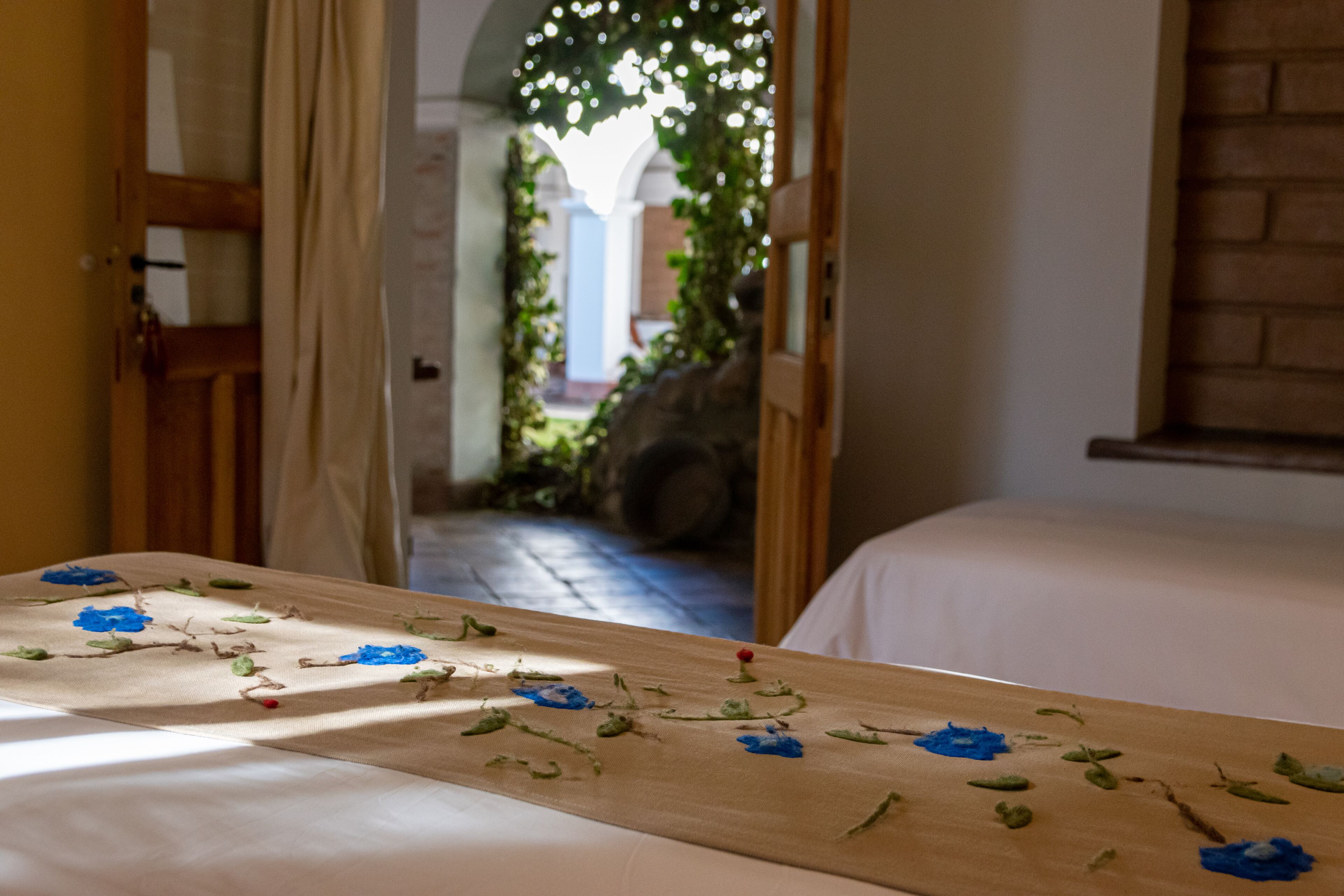 A room with a bed, a wooden table with painted flowers, and a view of a courtyard through an open door.