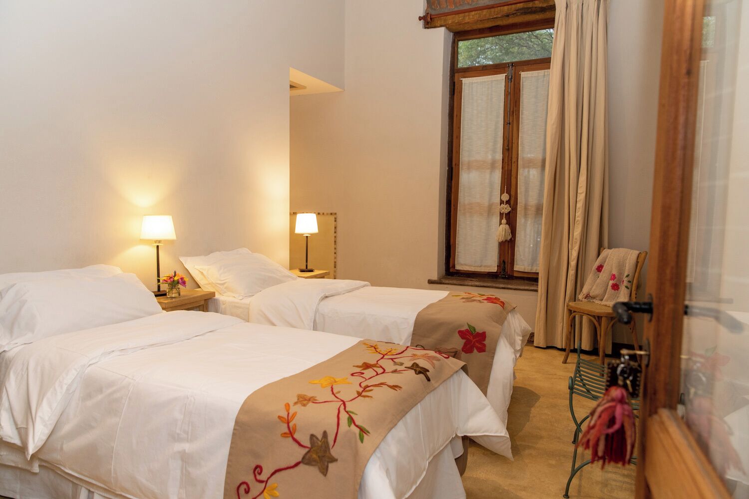 A hotel room with two beds, a window with curtains, a chair, and a nightstand with a lamp.