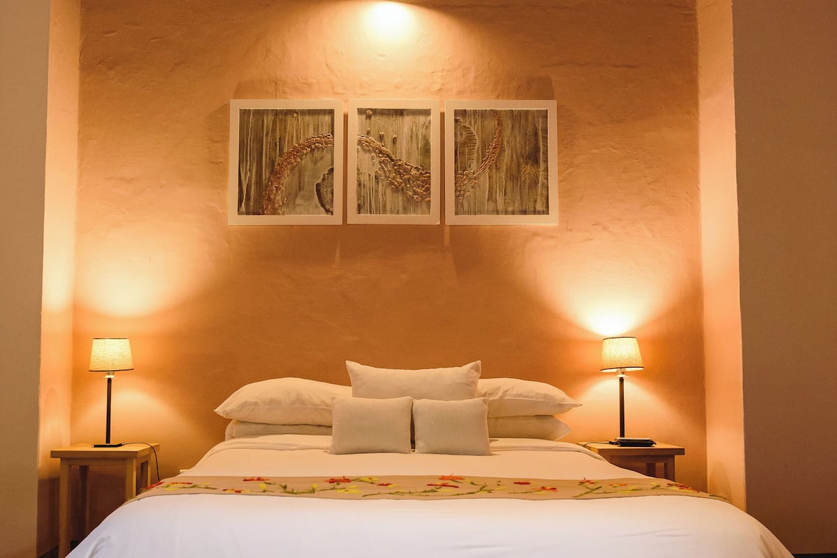 A bedroom with a large bed, two bedside lamps, and a mural on the wall.