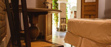 A room with a bed, a wooden chair, a table, and a doorway leading to another room.