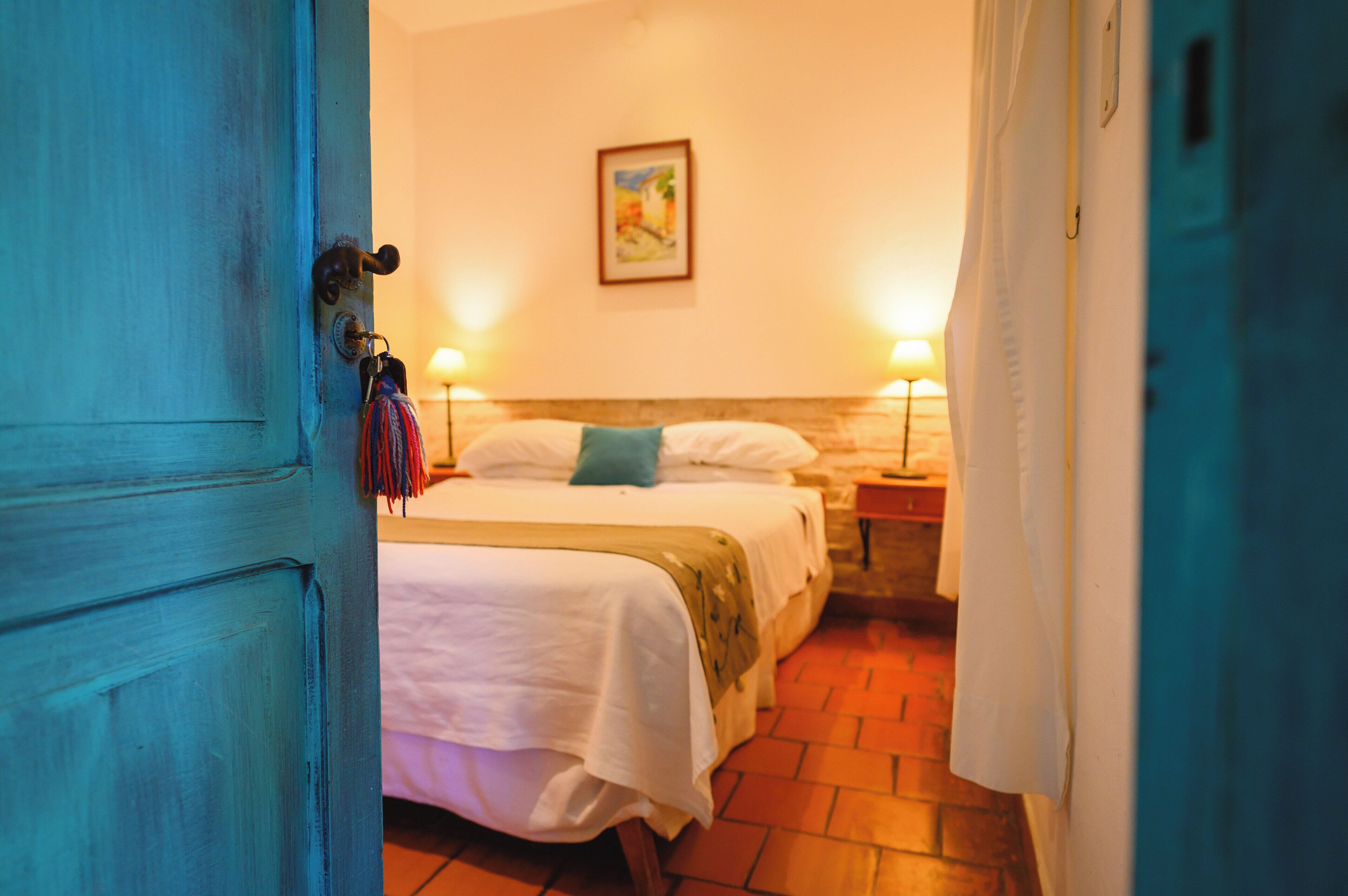 A room with two beds, a painting on the wall, and a door with a key hanging on it.