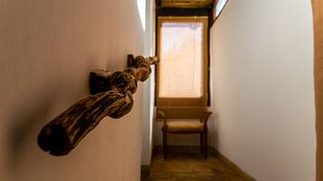 Un pasillo estrecho con una escultura de madera en la pared, una silla de madera y una ventana con luz natural.