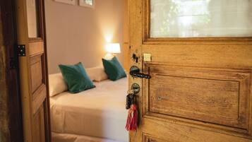 Een houten deur met een sleutelgat en sleutelhanger, die leidt naar een slaapkamer met een bed, kussens en een nachtkastje met een lamp.