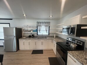 A modern kitchen with white cabinets, a stainless steel refrigerator, a black stove, and a microwave.