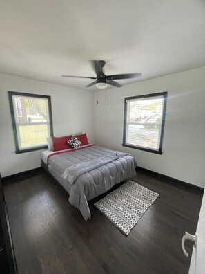 A bedroom with a bed, a ceiling fan, two windows, and a patterned rug.