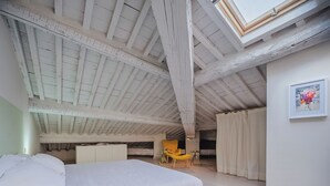 A bedroom with a large bed, a chair, a desk, and a skylight.