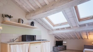 A compact kitchen with a microwave, sink, and wooden cabinets. There are skylights and a window providing natural light.