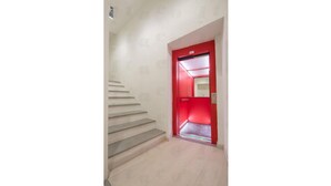 A staircase leading to a red door with a mirror and a light fixture above it.