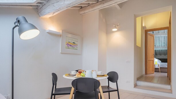 A dining area with a round table, black chairs, a floor lamp, and a painting on the wall.
