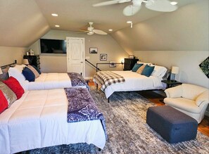 Cozy attic bedroom with two double beds, a sofa, and a nightstand, featuring framed pictures and a window.