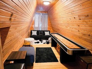 A small, wooden-paneled room with a bed, a bench, a table, and a sofa.