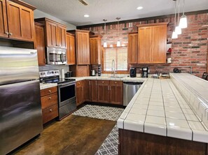 Kitchen features a large island with a sink and a dishwasher, along with a brick wall and window.