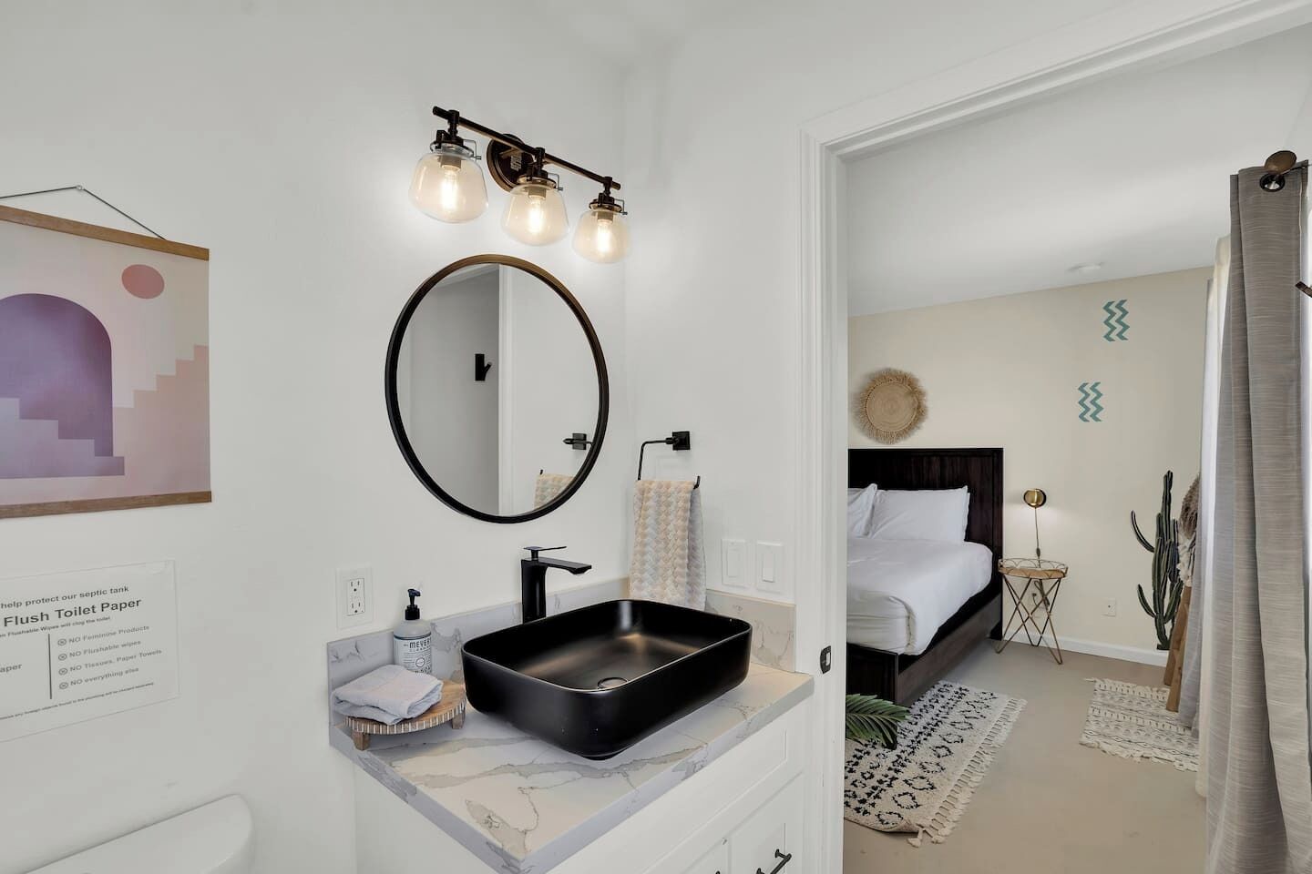 A modern bathroom with a black sink, a round mirror, and a wall-mounted light fixture.