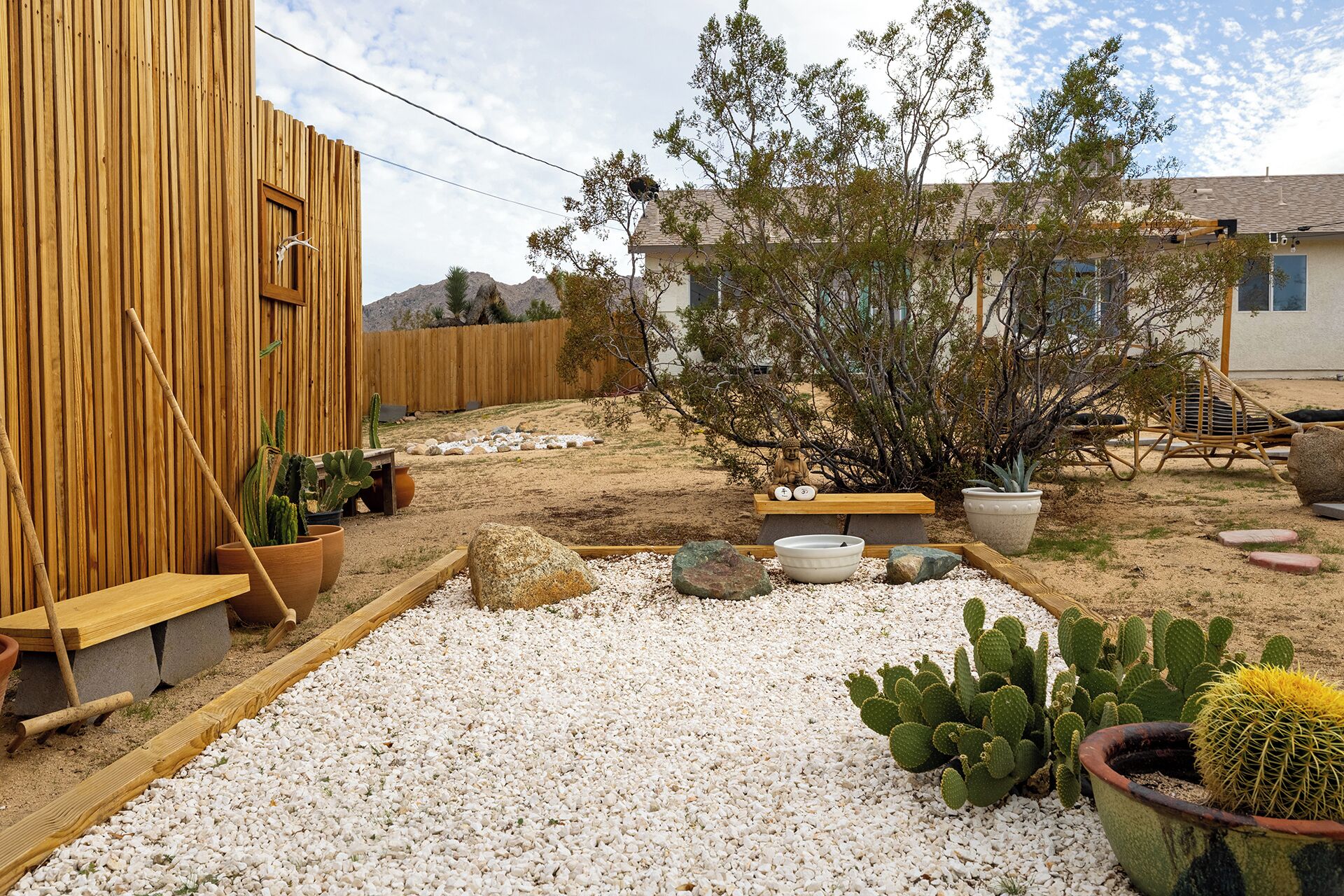 Un jardín con valla de madera, una estatua de Buda y diversos cactus.