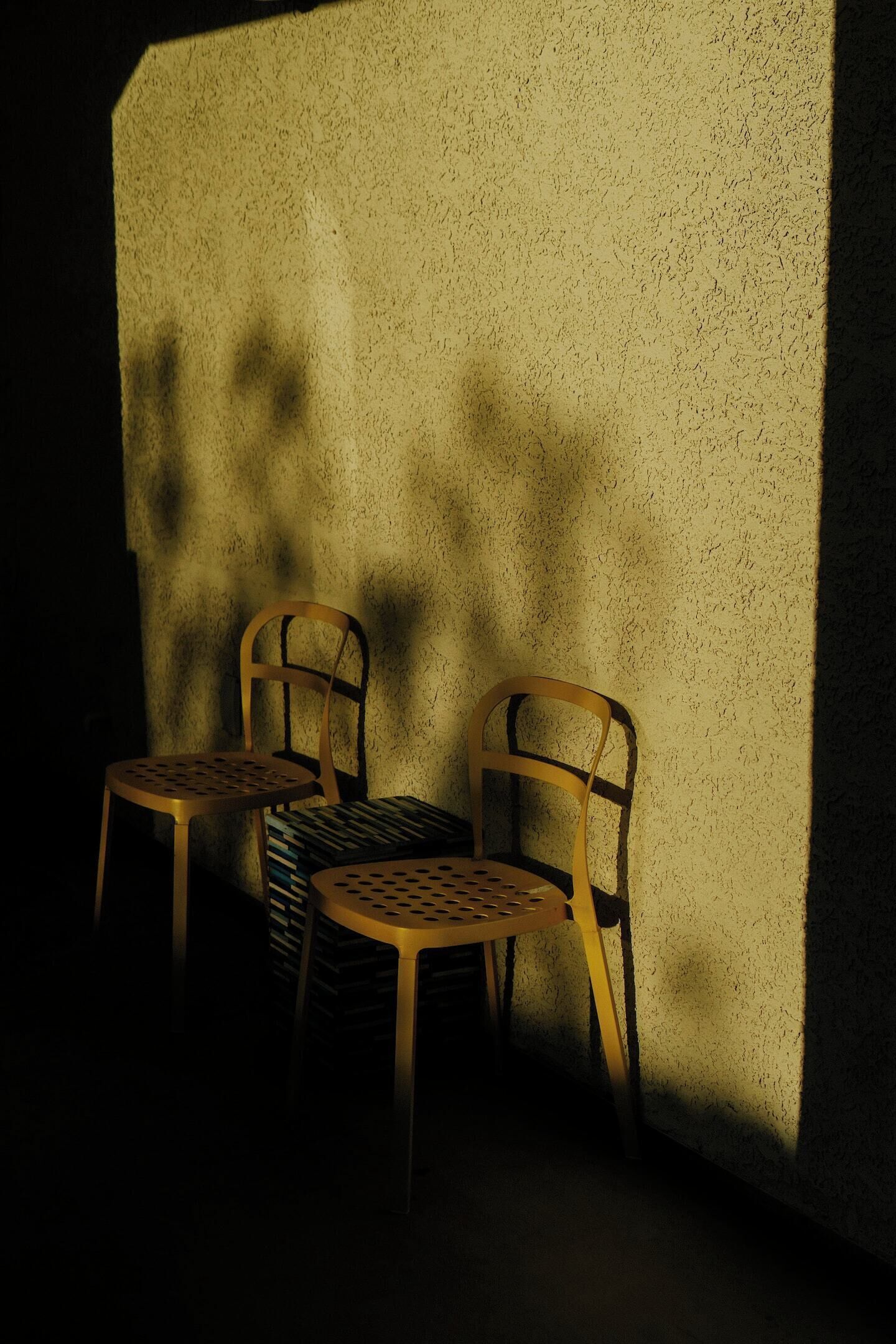 Two wooden chairs with metal frames and a woven seat, positioned against a textured wall.