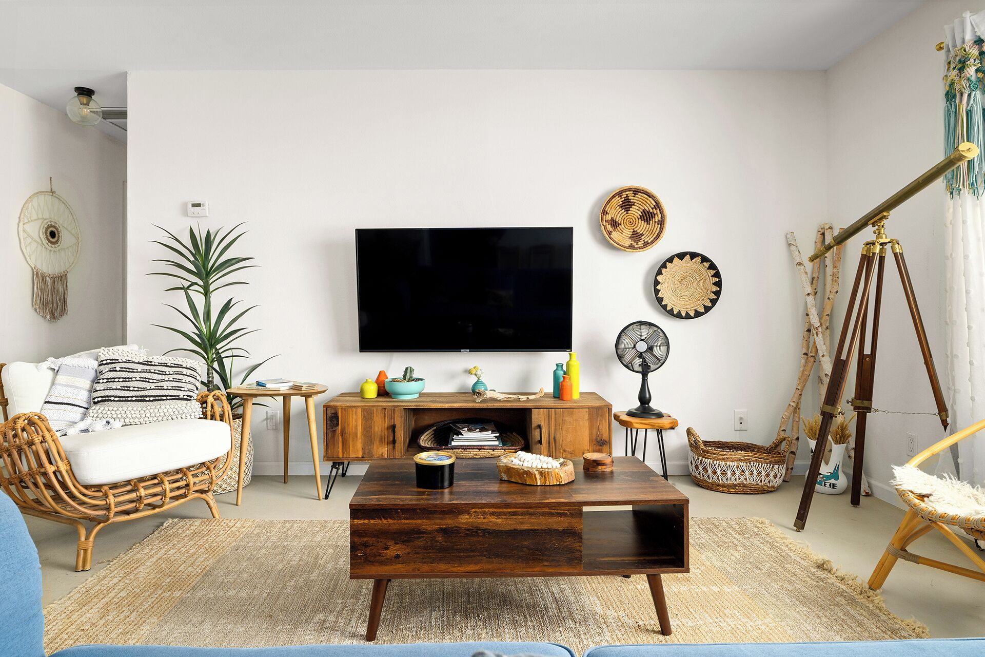 Un salon doté d’un téléviseur à écran plat, d’une table basse en bois, de meubles en osier et d’œuvres d’art décoratives accrochées au mur.