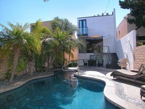 A modern house with a swimming pool, palm trees, and a balcony.