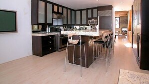 Een moderne keuken met donkere kastjes, een centraal eiland met barstoelen en een eethoek.