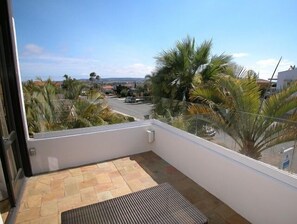 A balcony with a stone floor, a view of a residential area, and palm trees.