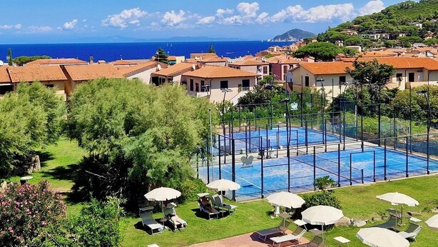 A resort with a large swimming pool, surrounded by lush greenery and red-roofed villas. - Resort Hotel Tamerici (Marciana Marina)