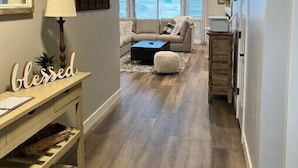 A narrow hallway with a wooden floor leading to a living area with a sofa and a coffee table. There is a lamp on a wooden console table, a sign that reads "blessed," and a ceiling fan. - Spectacular Mesa view 3 room home  (Grand Junction)