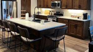 A modern kitchen with a central island, bar stools, wooden cabinets, stainless steel appliances, and pendant lighting. - Spectacular Mesa view 3 room home  (Grand Junction)