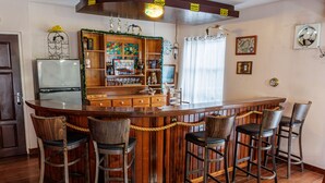 Een bar met houten barstoelen, een houten toonbank en een decoratieve plank met diverse objecten.