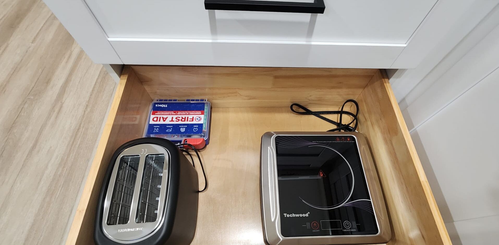 A drawer containing a toaster, a power strip, and a box of first aid supplies.