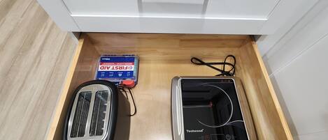 A drawer containing a toaster, a power strip, and a box of first aid supplies.
