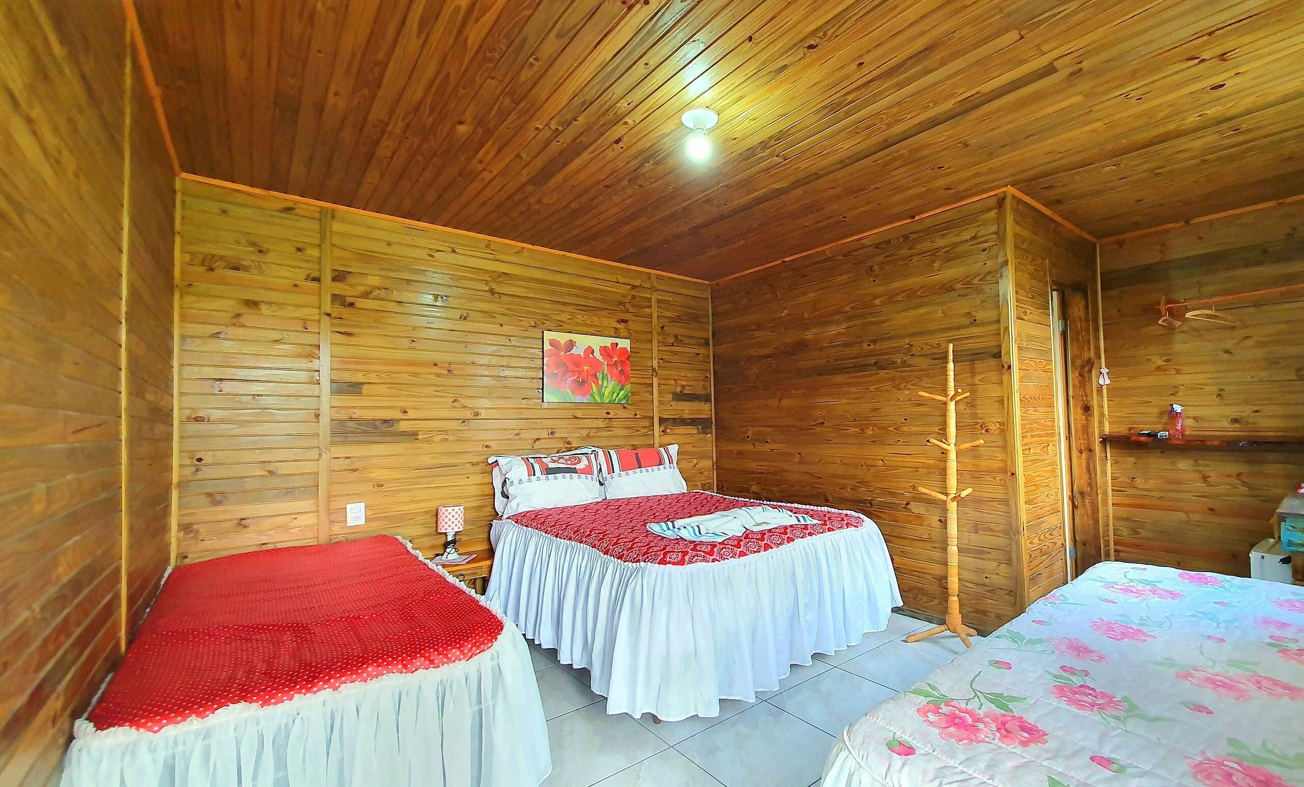 A wooden cabin room with two beds, a wooden ceiling, and a wall-mounted light fixture.