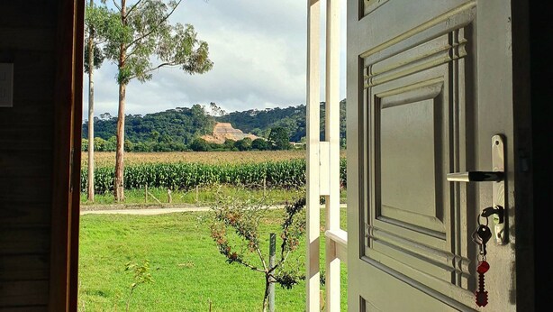 A view from inside a building, looking out to a green field with a tree and a hill in the distance. - Pousada Mato Verde - Urubici - SC (Urubici)