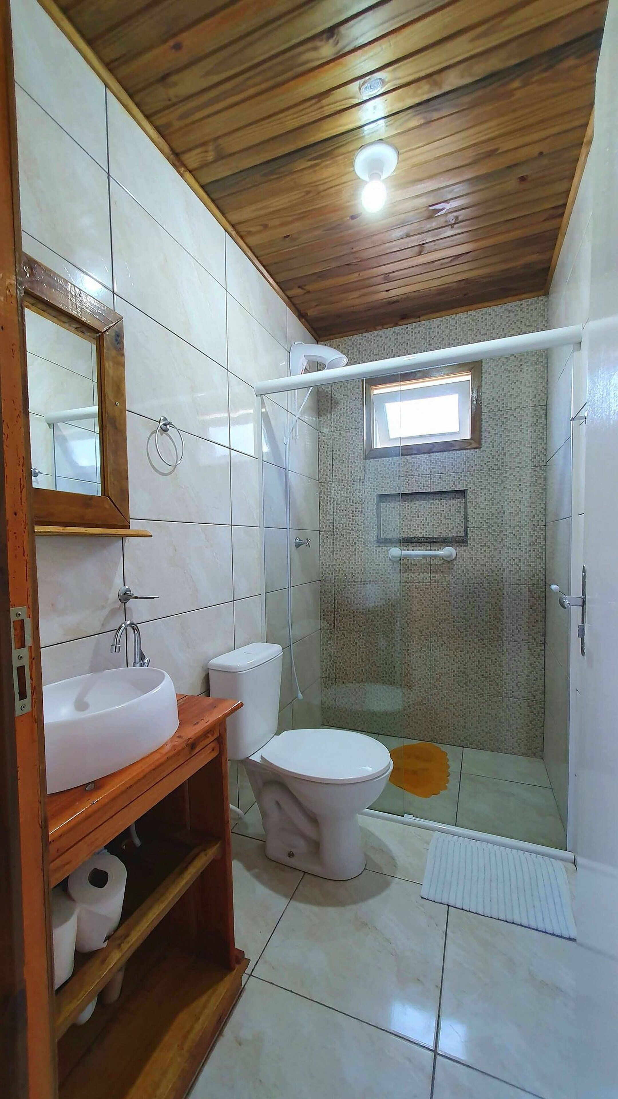 A bathroom with a wooden ceiling, a white sink, a toilet, and a glass-enclosed shower area.
