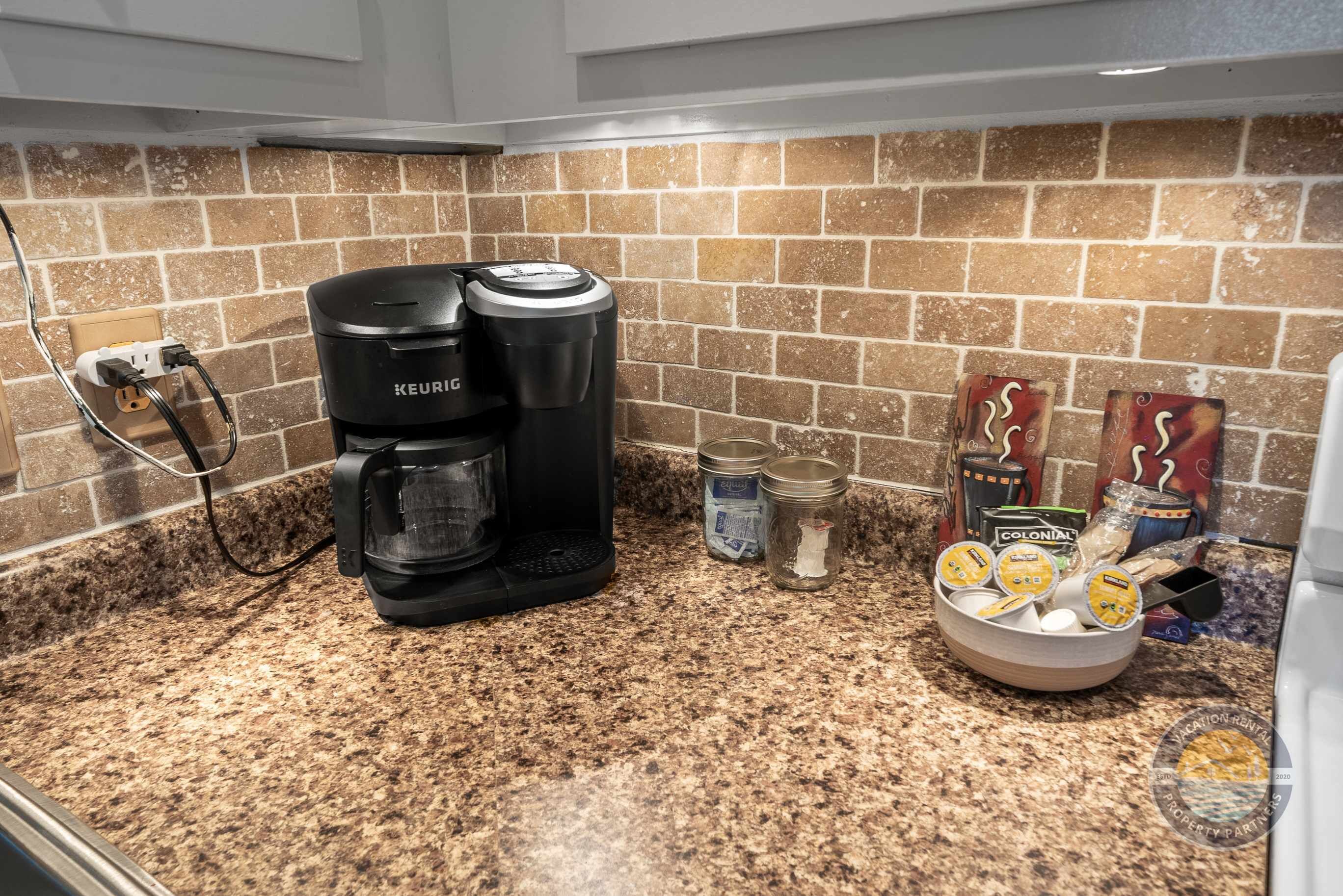 A kitchen with a Keurig coffee maker, a bowl of coffee pods, and some jars on the counter.
